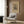 May include: Abstract geometric art print in warm beige and black tones displayed above a modern cream armchair with geometric patterned pillow. Vintage-style poster features intersecting lines, shapes, and patterns in Kandinsky's distinctive style, framed in light wood against wood-paneled wall. Golden floor lamp and dark side table with open book complete the contemporary reading nook setting with natural lighting from nearby window.