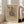 May include: Framed abstract geometric art print with black angular shapes, lines, and patterns on beige textured background, displayed in light wooden frame leaning against white wall corner next to beige upholstered chair in bright modern living room with large windows and natural sunlight streaming across hardwood floors.