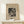 May include: Framed abstract art print by Wassily Kandinsky featuring geometric shapes, circles, and linear elements in black ink on cream paper, displayed on light wood surface beside small white gift box with twine and evergreen sprig against neutral wall