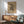 May include: Abstract geometric artwork by Wassily Kandinsky displayed in wooden frame on white wall above mid-century modern credenza. Print features black line drawings and shapes on beige background. Scene shows mint green upholstered chair with wooden arms, white ceramic table lamp, and natural lighting creating shadows across the minimalist interior setting.