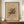 May include: Framed abstract art print with colorful geometric shapes and lines in yellow, blue, red, and green on beige background, displayed on wooden sideboard next to white ceramic vase and stack of books in modern interior with cream walls and white molding.
