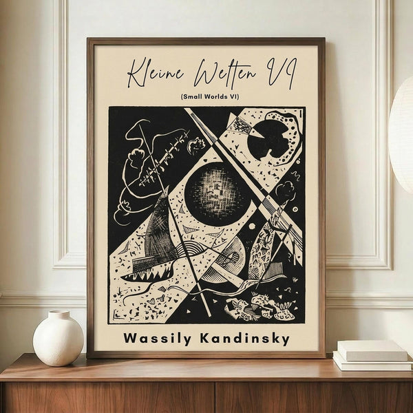 May include: Framed abstract art print in black and white featuring geometric shapes, curved lines, and cosmic elements including what appears to be a moon or planet. The artwork shows Kandinsky's distinctive abstract style with various patterns and textures. Displayed on a wooden sideboard alongside a white ceramic vase and stacked books in a modern interior with cream walls and white trim.