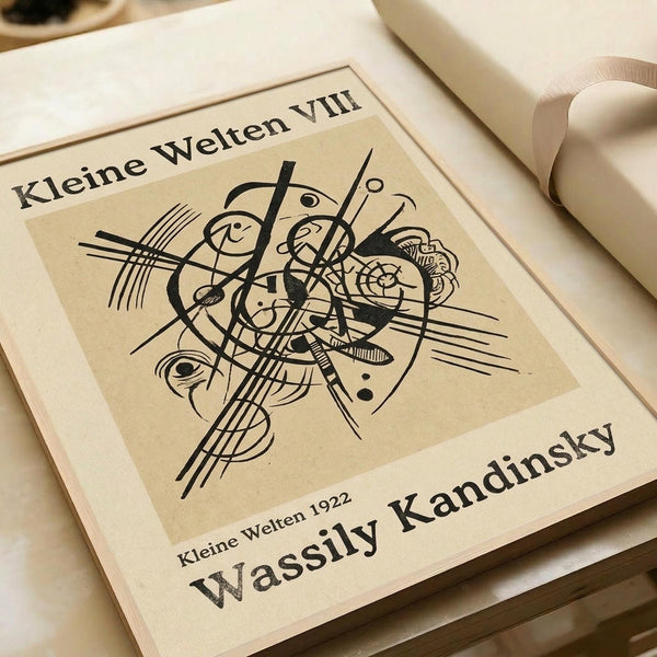 Abstract geometric composition with black curved lines, circles, and angular shapes on beige background. The artwork features flowing organic forms intersected by straight lines and musical notation-like elements. Print is displayed in an open book or portfolio with cream-colored pages against white rolled paper tubes, creating an artistic flat lay arrangement.