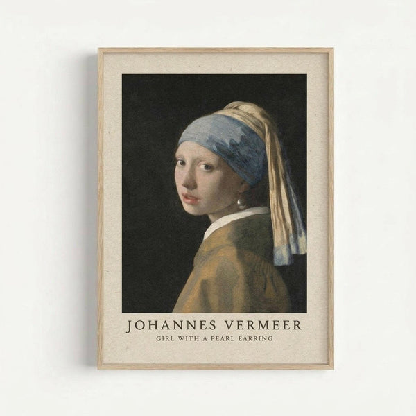 May include: Framed reproduction of Vermeer's Girl with a Pearl Earring displayed on white wall. Light wood frame surrounds cream matted print showing young woman in blue and yellow turban with pearl earring against dark background. Title text below image reads "Johannes Vermeer Girl with a Pearl Earring" in serif font.