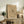 May include: Framed abstract art print with black linear geometric shapes and dots on beige background, displayed on rustic wooden sideboard alongside fern plant, ceramic vase, and books in neutral-toned living room setting with cream chair visible