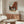 May include: A framed art print featuring Vermeer's painting of Dutch buildings with red brick facades and a cobblestone courtyard under a cloudy sky. The poster hangs above a mid-century modern walnut credenza in a minimalist living room with white walls, accompanied by a cream upholstered chair, brass floor lamp, glass coffee table, and white table lamp.