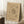 May include: Framed beige art print with black abstract geometric designs and scattered dots, leaning against white wall next to wooden block with coffee cup and saucer, on white textured rug with beige blanket visible at edge