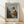 May include: Framed art print of Vermeer's classical painting showing a young woman in golden yellow and white dress seated at virginals, looking over her shoulder. Natural wood frame with cream matting, displayed on light wooden floor against white wall with soft natural lighting creating diagonal shadows.