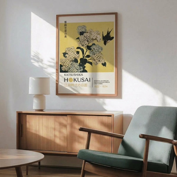 May include: A framed Japanese art print featuring white hydrangea flowers and a black bird on yellow background, displayed on white wall above wooden sideboard. Mid-century modern mint green armchair with wooden arms sits nearby, along with white ceramic table lamp and round wooden coffee table. Natural sunlight creates geometric shadows across the minimalist room setting.