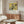May include: Japanese art poster featuring white hydrangea flowers and black bird on yellow background, displayed in thin brown frame above wooden sideboard. Modern living room setting with cream chair, glass oval coffee table, and floor lamp. Clean minimalist interior with neutral walls and natural lighting.