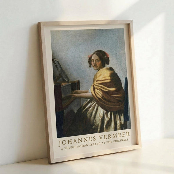 May include: Framed art print reproduction of classical painting showing woman in golden-yellow draped clothing seated at virginals keyboard instrument, looking over shoulder toward viewer. Artwork features muted blue-gray background, realistic Renaissance painting style. Natural wood frame with white mat, leaning against white wall with soft natural lighting casting subtle shadows.