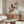 May include: Japanese-style bird artwork print displayed above a walnut wood sideboard in a modern living room. The vintage-style poster features two colorful birds with red and blue plumage perched on branches against a cream background. Room styled with white sculptural chair, glass-top coffee table, and white table lamp.