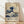 May include: Framed reproduction of Hokusai's famous Great Wave woodblock print displayed against white wall on wooden floor. The artwork shows a large blue wave with white foam threatening boats, with Mount Fuji visible in background. Poster features exhibition-style text reading "Katsushika Hokusai 1830-1833" and Japanese characters on cream-colored paper in simple wooden frame.
