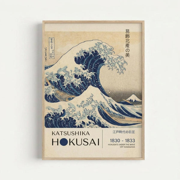 Framed reproduction of Hokusai's famous Great Wave woodblock print showing a large blue and white wave with foam and spray threatening boats, with Mount Fuji visible in the background. The print includes Japanese text and exhibition-style labeling reading "KATSUSHIKA HOKUSAI 1830-1833" at the bottom. The artwork is displayed in a light wooden frame against a white wall, showing the classic ukiyo-e art style with deep blue pigments and flowing wave forms.