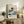 May include: Framed poster of Hokusai's famous blue wave artwork with Japanese text and exhibition details, displayed on rustic wooden sideboard alongside fern plant, books, and ceramic vase in neutral-toned living room setting