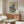 May include: Japanese-style waterfall poster with blue cascading water, red-orange rocks, and green foliage displayed above a wooden sideboard. Modern living room setting features white curved chair, glass oval coffee table, and neutral walls. The framed artwork shows traditional woodblock print styling with bold colors and flowing water elements.
