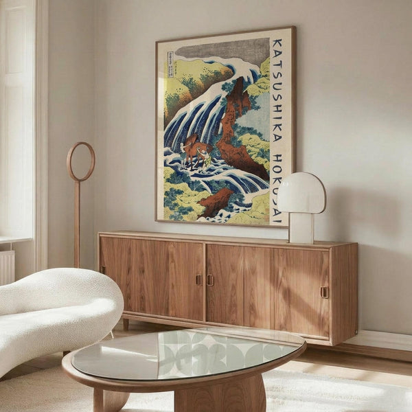 May include: Japanese-style waterfall poster with blue cascading water, red-orange rocks, and green foliage displayed above a wooden sideboard. Modern living room setting features white curved chair, glass oval coffee table, and neutral walls. The framed artwork shows traditional woodblock print styling with bold colors and flowing water elements.