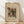 May include: A framed abstract art print by Wassily Kandinsky titled "Small Worlds V" leaning against a white wall on light wooden flooring. The artwork features geometric shapes, lines, and patterns in black, red, yellow, and teal on cream paper. Natural lighting creates soft shadows across the scene. The wooden frame has a natural finish and the print shows Kandinsky's characteristic abstract expressionist style with scattered dots, crosshatched patterns, and dynamic angular forms.