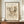 May include: Abstract modernist artwork print in warm brown frame, displayed on wooden sideboard against cream paneled wall. Features dynamic abstract forms with cross-hatching, geometric patterns, and flowing lines in sepia tones on aged paper background. White ceramic vase and stacked books create styled vignette beside the framed print.