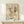 May include: Abstract artwork print in light wooden frame showing dynamic black line drawings and organic shapes on cream background. Framed poster leans against white wall on light wood surface next to small white gift box with greenery sprig. Minimalist modern home decor styling with natural lighting and neutral tones throughout the scene.
