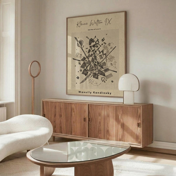 May include: Abstract black and white geometric artwork by Wassily Kandinsky displayed above a mid-century modern walnut credenza in a minimalist living room. The framed print features dynamic intersecting lines, shapes, and patterns on cream paper. Room has white curved chair, glass oval coffee table, copper floor lamp, and white table lamp with warm natural lighting.