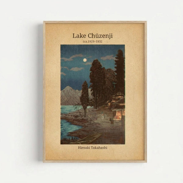 Framed vintage Japanese woodblock print showing a moonlit evening scene at a lake with mountains in the background. The artwork features a traditional building with warm glowing lights, tall dark trees, and small figures on a path beside turquoise water. The print has a beige mat with text identifying it as Lake Chuzenji by Hiroaki Takahashi, circa 1929-1932, all enclosed in a natural wood frame against a white wall.