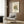 May include: Abstract Kandinsky poster with geometric shapes in orange, teal, black and beige, displayed in white frame on wood paneled wall above beige upholstered chair with geometric patterned pillow. Modern brass floor lamp and dark round side table with open book complete the warm, contemporary room setting with wood floors and white curtains.