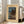 May include: Framed vintage Japanese woodblock print showing a moonlit lakeside scene with traditional buildings, tall trees, mountains, and blue water. The artwork has a cream-colored mat border and white frame, leaning against a white wall next to a beige sectional sofa in a bright living room with hardwood floors and large windows.