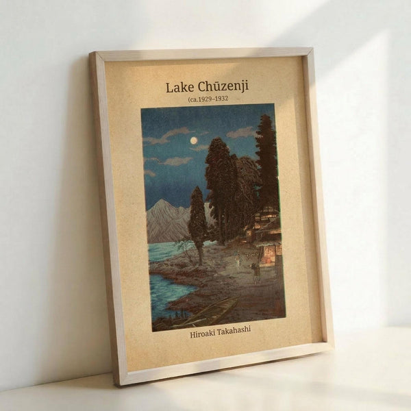 May include: Framed vintage Japanese woodblock print reproduction showing a moonlit lakeside scene with traditional buildings, tall cypress trees, mountains, and turquoise water. The artwork features a cream-colored mat with text identifying the piece and artist. The wooden frame leans against a white wall, displaying the classic blue and earth-toned night landscape in traditional Asian art style.