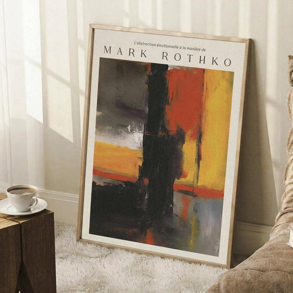 May include: Framed abstract art print leaning against white wall in cozy room setting. Artwork features bold blocks of yellow, orange, red, and black paint with soft, blurred edges in Rothko's signature style. Light wooden frame surrounds the poster. Scene includes white coffee cup on wooden block side table, cream textured rug, and beige throw blanket. Natural sunlight creates soft shadows on the wall.