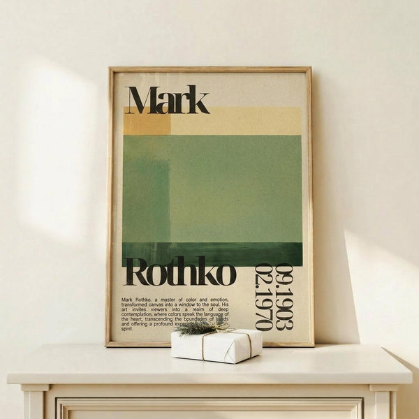May include: Framed poster with Mark Rothko's name in bold black letters above abstract color blocks in cream, yellow, and varying shades of green. Text below describes the artist with birth and death dates. Natural wood frame sits on light wooden surface next to small white wrapped gift with twine and greenery sprig against cream wall.