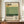 May include: A framed poster featuring abstract color blocks in cream, yellow, and green tones with "Mark Rothko" text and biographical information, displayed on a wooden sideboard next to a white ceramic vase and books in an elegant room with white paneled walls.