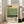 May include: Framed poster with Mark Rothko's name at top in black text, horizontal bands of cream, yellow and green colors in center, "Rothko" and birth/death dates below, with descriptive text about the artist at bottom. Light wood frame leaning against white wall near beige couch in bright room with large windows.