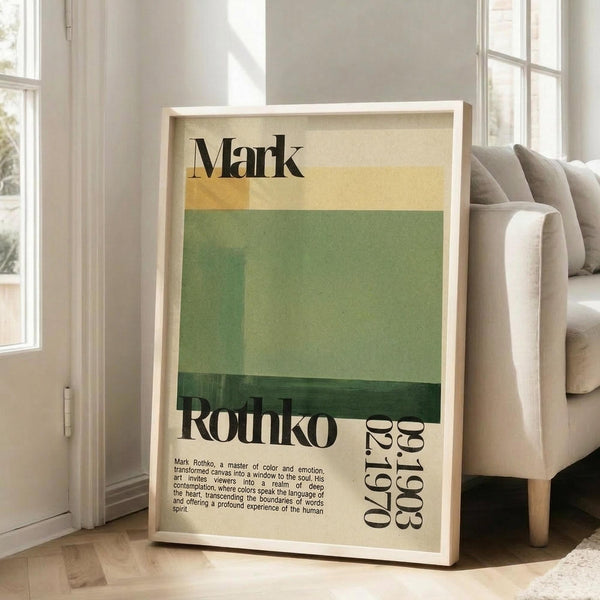 May include: Framed poster with Mark Rothko's name at top in black text, horizontal bands of cream, yellow and green colors in center, "Rothko" and birth/death dates below, with descriptive text about the artist at bottom. Light wood frame leaning against white wall near beige couch in bright room with large windows.