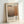 May include: Framed poster print featuring abstract geometric shapes in warm earth tones - beige, tan, and orange rectangular blocks. Black text displays "Mark Rothko" at top and "1903-1970" vertically on right side. Small descriptive paragraph about the artist appears at bottom. Light wood frame sits against white wall on neutral surface, showing gallery-style presentation.