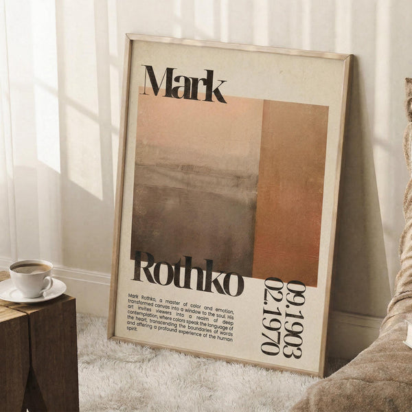 May include: Framed poster leaning against white wall featuring abstract earth-toned rectangular color blocks in cream, peach, and brown gradients with "Mark Rothko" text and biographical information below. Scene shows coffee cup on wooden side table, white furry rug, and beige fabric chair in soft natural lighting.