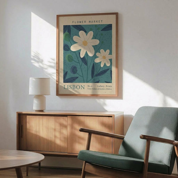 May include: Framed botanical poster featuring white daisies with yellow centers against teal blue background with green leaves, displayed above wooden sideboard with ceramic lamp in modern living room setting. Mid-century style chair with sage green upholstery and wooden arms visible in corner. Natural sunlight creates shadows on white wall.