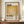 May include: Framed art print featuring Mark Rothko's name in bold black letters above a golden yellow rectangular color field on cream background, with biographical text and dates below. Wooden frame displayed on walnut credenza beside white ceramic vase and stacked books against beige wainscoted wall.