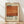 May include: Framed poster print with cream background featuring large orange-red abstract rectangular color block. Black text reads "Mark Rothko" with years "02.1970" vertically along right side. Small descriptive paragraph appears at bottom left. Wooden frame sits on light wood floor against white wall with soft natural lighting creating diagonal shadows.