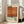 May include: Framed vintage-style poster with cream and orange color blocks, featuring "Mark Rothko" text and biographical description. White wooden frame leaning against white wall corner next to beige upholstered sofa with pillows. Bright natural light streams through tall windows onto hardwood floors with area rug in minimalist living room setting.