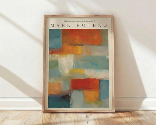 May include: Framed abstract art print in light wood frame leaning against white wall on wooden floor. Artwork features soft rectangular blocks of color including orange, red, blue, yellow, and white with painterly, blended edges in style reminiscent of Mark Rothko. Natural lighting creates diagonal shadows across the scene. Frame appears medium-sized relative to baseboard and flooring.
