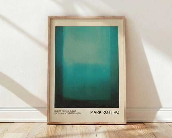 May include: Framed poster print of abstract color field artwork featuring gradient turquoise and teal tones transitioning to darker green-black at bottom, displayed in light wood frame against cream textured wall with natural lighting creating diagonal shadows across wooden floor.