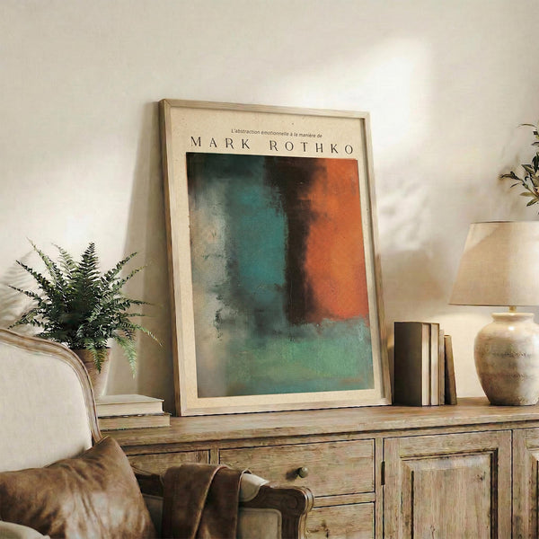 May include: Framed abstract art print with teal, orange, and dark color blocks in Rothko style, displayed on rustic wooden sideboard alongside fern plant, ceramic vase, and books in neutral-toned living room setting with beige chair and cream walls