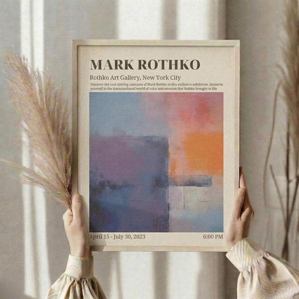 May include: Hands holding a framed beige poster featuring an abstract artwork with blue, orange, pink and purple rectangular color blocks. The poster shows exhibition text and dates. Dried pampas grass stems are held alongside the frame. Person wears a cream colored top with gathered sleeves against soft neutral curtained background.