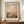 May include: Framed abstract art print in warm orange, pink and brown tones with Mark Rothko text at bottom, displayed on wooden sideboard beside white ceramic vase and stacked books in elegant room with cream walls and white molding.