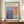 May include: Framed exhibition poster featuring Mark Rothko's abstract artwork with soft blocks of blue, purple, orange, and cream colors. The poster displays gallery information and exhibition dates, shown in a brown wooden frame on a wooden credenza alongside a white ceramic vase and stacked books in a bright interior setting with white paneled walls.
