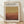 May include: Framed exhibition poster with Mark Rothko's name in bold black letters at top, featuring abstract color field artwork transitioning from golden yellow at top to deep reddish-brown at bottom. White matting surrounds the design with exhibition details and dates below. Light wood frame displayed on wooden floor against cream wall with soft window lighting creating diagonal shadows.