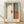 May include: Framed abstract art print in light wood frame leaning against white textured wall on light wooden floor. Artwork features vertical composition with muted blue-green, cream white, dark brown, and rust orange color blocks in soft, blended style. French text below image reads "L'abstraction émotionnelle à la manière de Mark Rothko" above "MARK ROTHKO" in brown lettering. Natural lighting creates gentle shadows on wall.