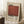 May include: Framed art print featuring Mark Rothko's name and dates (1903-1970) with a large rust-red rectangular color block on cream background. The vintage-style poster leans against a white wall near a wooden side table with coffee cup, alongside a textured throw blanket on a white fluffy rug.