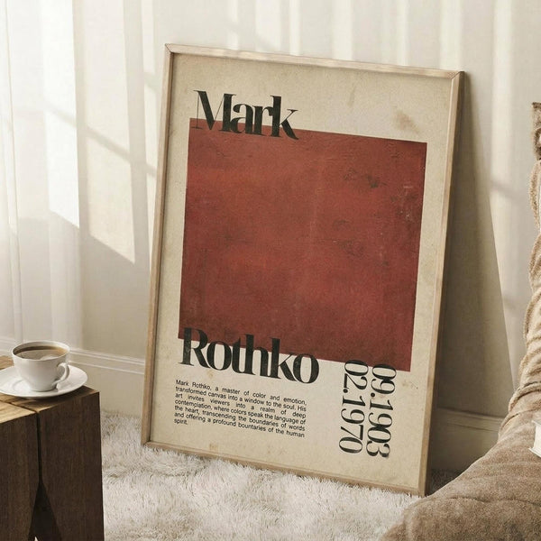 May include: Framed art print featuring Mark Rothko's name and dates (1903-1970) with a large rust-red rectangular color block on cream background. The vintage-style poster leans against a white wall near a wooden side table with coffee cup, alongside a textured throw blanket on a white fluffy rug.